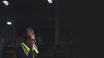 Trabajador de almacén usando un teléfono en un espacio industrial con poca luz