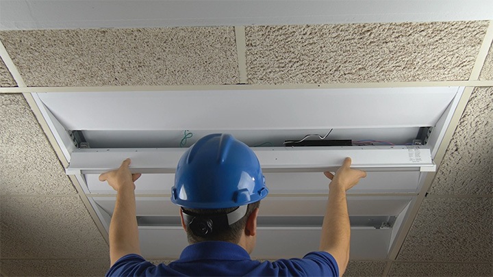 Man with blue hard hat installing lighting in ceiling