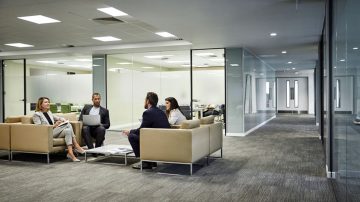Four colleagues having a conversation on cream sofas in a modern glass-partitioned office