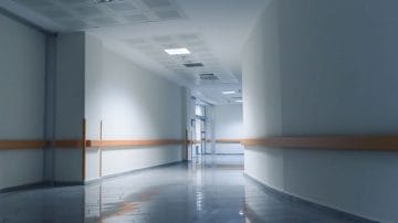 An empty hospital corridor with white walls, wooden handrails, and a polished reflective floor