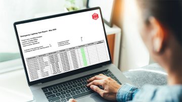 A person reviewing an emergency lighting test report on a laptop screen.