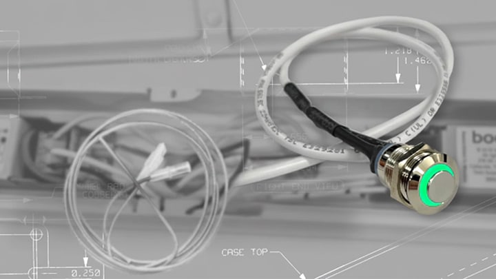 Close-up of a metal ABConnect enable connector with a glowing green indicator ring, with coiled wiring and a Bodine emergency driver visible in the background