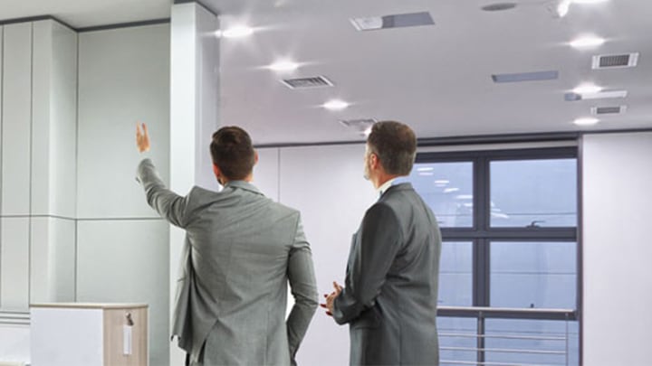 Two professionals in a modern office space, with one pointing up at the ceiling lighting installation, with a spiral staircase visible in the background