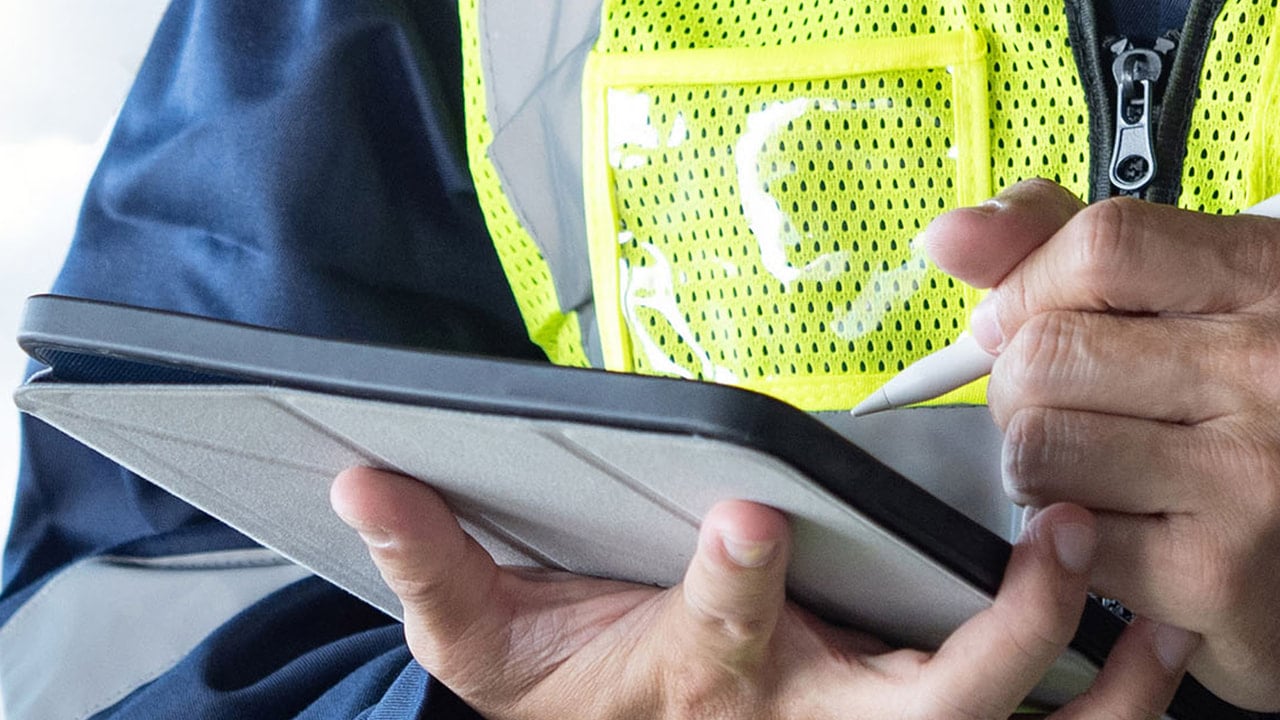 A close-up of a worker in a high-visibility vest using a stylus on a tablet
