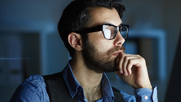Man wearing glasses looking at a screen in a dark environment