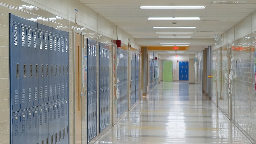 An empty school corridor lined with blue lockers, lit by fluorescent ceiling lights stretching into the distance