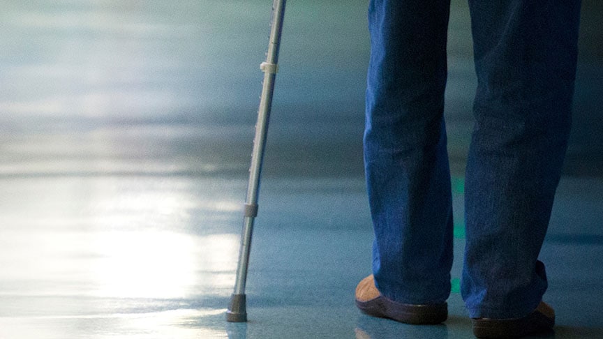 A person walking with a cane along a dimly lit corridor with a reflective floor