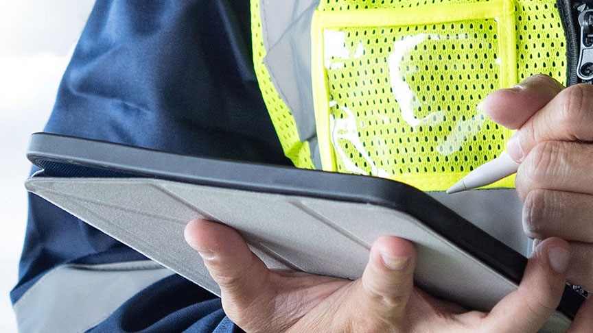 A close-up of a worker in a high-visibility vest using a stylus on a tablet