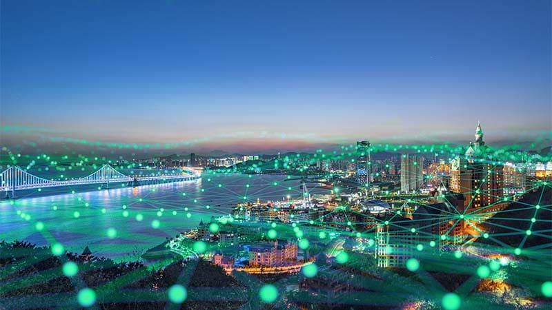 An aerial view of a lively city with interconnected green dots above, showcasing a network of sustainable energy initiatives.