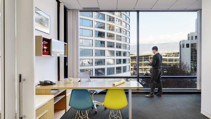 Person standing by a large office window, looking out over city buildings.
