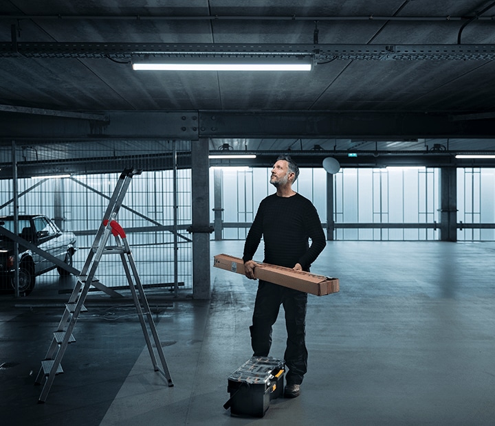Man in een opslagruimte onder een LED-lamp, naast een ladder en een gereedschapskist.