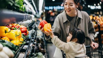 Woman grocery shopping with child in a brightly lit supermarket